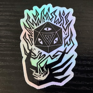 May include: A black and white sticker with a holographic finish. The sticker features a stylized image of a hand holding a d20 die with three eyes. The die is surrounded by flames.