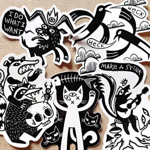 Può includere: Una collezione di sei adesivi in vinile bianco e nero con varie illustrazioni, tra cui una capra con il testo I DO WHAT I WANT, uccelli che dicono HECK, un procione e un opossum con un teschio, un gatto con una lisca di pesce e una moffetta.