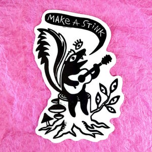 May include: Black and white sticker of a cartoon skunk playing a guitar with the text "Make a Stink" above it.