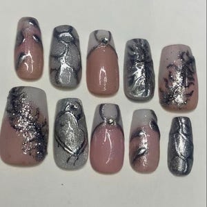 Puede incluir: Un juego de diez uñas postizas con una mezcla de diseños en tono nude y plateado. Algunas uñas tienen remolinos metálicos plateados, otras presentan una base nude con puntas plateadas y dos incluyen pequeños diamantes de imitación.