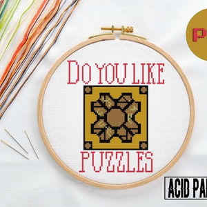 May include: A cross-stitch pattern featuring a pixelated image of a puzzle piece with the text "Do you like puzzles?" in red. The pattern is on a white background and is framed in a wooden hoop. The image also includes a small logo for Acid Panda.