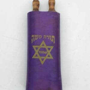 May include: A purple Torah scroll with wooden handles. The scroll features gold Hebrew text and a gold Star of David with the word "TORAH" inside. The scroll is rolled up and ready to be read.