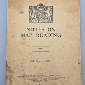 May include: A vintage 1929 softcover booklet titled Notes on Map Reading by The War Office. The tan cover features a black royal coat of arms, text detailing publication by His Majesty's Stationery Office, and handwritten ink at the top.