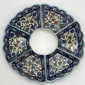 May include: A circular serving dish with six wedge-shaped compartments. Each section features a floral pattern in blue, brown, and green on a cream background, framed by a scalloped edge and a blue border. The dish is designed for serving appetizers or snacks.