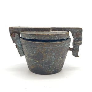 May include: A small, antique, hinged, brass container with a patina finish. The container has a rounded, cylindrical shape and a hinged lid.