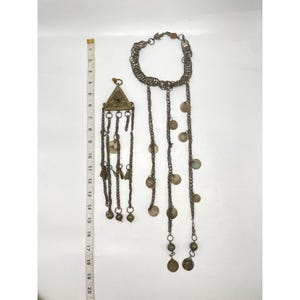 Può includere: Una collana in argento e oro con un ciondolo triangolare e più catene con ciondoli a forma di moneta. La collana è lunga circa 50 cm.