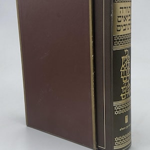 May include: A brown hardcover book with a matching slipcase. The spine features gold-colored Hebrew text and decorative geometric patterns, including Star of David motifs. The cover is plain brown with a thin gold border along the edges.