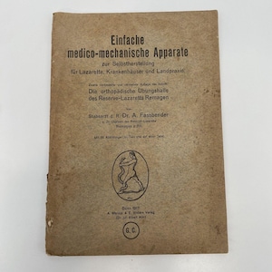 Puede incluir: Una cubierta de libro de color beige con el título "Einfache medico-mechanische Apparate" en texto negro. El libro trata sobre la autoconstrucción de dispositivos médicos para hospitales y hospitales de campaña. La cubierta también incluye el nombre del autor, "Stabsarzt d. R. Dr. A. Fassbender", y la fecha de publicación, "Bonn 1917".