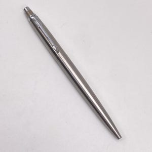 Puede incluir: Un bolígrafo de acero inoxidable cepillado con un diseño clásico de cuerpo cónico. El bolígrafo incluye un clip de bolsillo plateado pulido con forma de flecha, un mecanismo de botón en la parte superior y un acabado metálico liso.