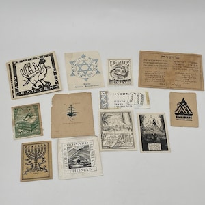May include: A collection of vintage Ex Libris bookplates, featuring diverse designs and text. The bookplates showcase illustrations of hands, stars, and other symbols, with text in multiple languages. The collection is arranged on a white surface.