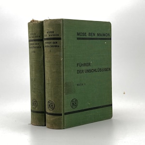 May include: Two vintage books with green covers. The spines and covers display the title "Führer der Unschlüssigen" and the author's name, "Mose Ben Maimon." The books have a worn appearance, suggesting age and use. The text is in German.