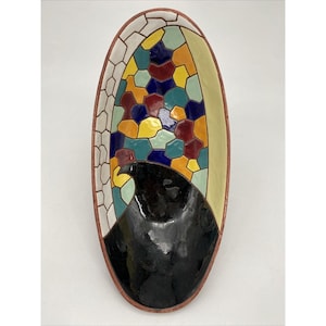 Pode incluir: Um prato oval de cerâmica com um desenho de pássaro preto e um padrão de mosaico colorido. O padrão de mosaico apresenta tons de vermelho, amarelo, azul, verde e branco.