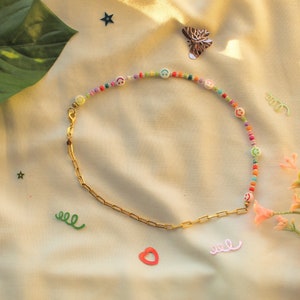 May include: A gold chain necklace with a colorful beaded section featuring smiley face charms. The beads are in shades of pink, blue, green, yellow, and orange.