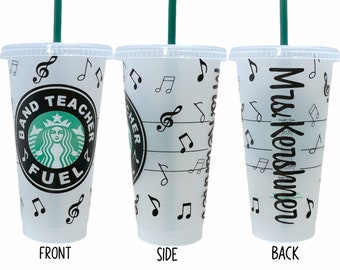 May include: A white reusable cup with a black and green Starbucks logo that says "Band Teacher Fuel". The cup is decorated with musical notes and a treble clef. The back of the cup says "Mrs. Konshomer".
