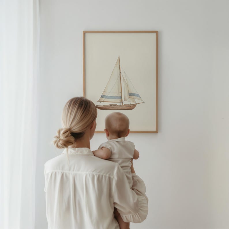 May include: A framed watercolor print of a sailboat with a beige background, light blue stripes, and a wooden frame. A person holds a baby in front of the artwork. The person is wearing a cream-colored button-down shirt.