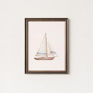 May include: Watercolor painting of a sailboat in a black and gold frame. The boat has a brown hull, white sails with blue stripes, and a light pink background. A nautical themed art print.
