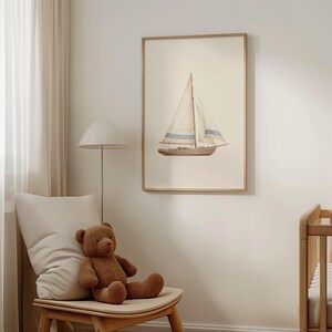 May include: A framed watercolor print of a sailboat with beige sails and blue stripes. The boat is brown and set against a cream background. The artwork is displayed in a light wood frame, suitable for a nursery or nautical-themed room.