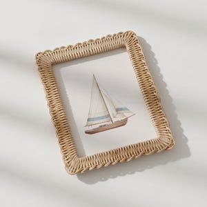 May include: A rectangular woven frame in a light beige color surrounds a watercolor painting of a sailboat. The sailboat has a brown hull, white sails with blue stripes, and a tall mast. The frame has a scalloped edge.