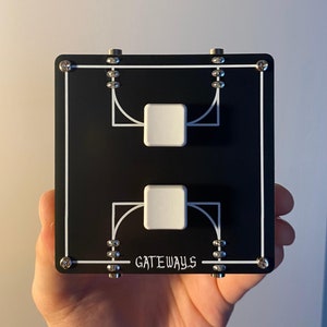 May include: A black square device with white lines and two white square buttons. The word "GATEWAYS" is printed in white. The device is held in a hand.
