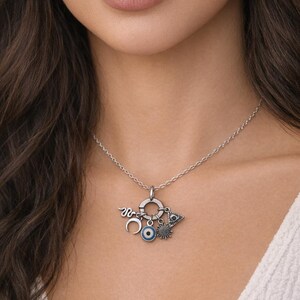 May include: Silver necklace with a pendant featuring a crescent moon, an evil eye, a sun, and a triangle. The necklace is worn by a person wearing a white top.