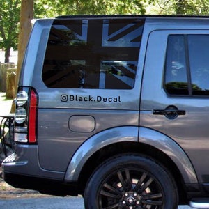 Könnte beinhalten: Ein grauer Land Rover Discovery mit einem schwarzen Union-Jack-Aufkleber auf der Heckscheibe. Der Aufkleber trägt den Text "@Black.Decal" darunter.