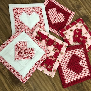 May include: Six handmade quilted pot holders with a heart design. The pot holders are made with red, white and pink fabrics with various patterns.