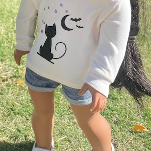 May include: White hoodie with a black cat silhouette, a crescent moon, and bats printed on the front. The cat is looking at the moon. There are purple glitter stars scattered around the design.