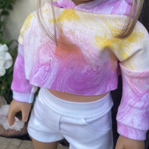 K&ouml;nnte beinhalten: Ein tie-dye-farbener, kurzer Hoodie mit langen &Auml;rmeln in den Farben Pink, Gelb und Wei&szlig;. Der Hoodie hat eine lockere Passform und einen l&auml;ssigen Stil.