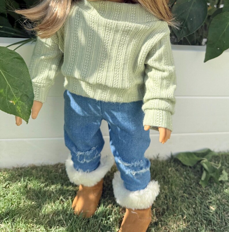 Puede incluir: Una mu&ntilde;eca con un su&eacute;ter verde claro y pantalones vaqueros azules con ribete de piel blanca en la parte inferior. La mu&ntilde;eca lleva botas marrones.