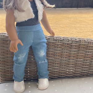 May include: A doll wearing a white faux fur vest, a gray tank top, blue denim jeans with distressed details, and white sparkly sneakers.