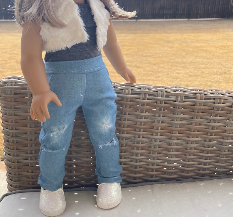 May include: A doll wearing a white faux fur vest, a gray tank top, blue denim jeans with distressed details, and white sparkly sneakers.