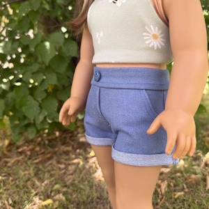 Peut inclure: Une poup&eacute;e v&ecirc;tue d'un haut court vert clair orn&eacute; d'un motif d'abeille et de marguerite, associ&eacute; &agrave; un short en jean bleu. Le short a un ourlet roul&eacute; et une fermeture boutonn&eacute;e. La tenue est con&ccedil;ue pour une poup&eacute;e.