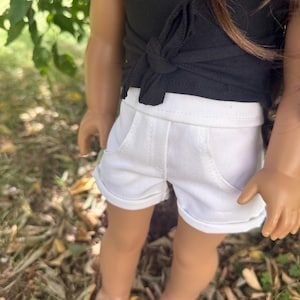 Peut inclure: Une poup&eacute;e v&ecirc;tue d'un haut noir nou&eacute; &agrave; la taille et d'un short blanc avec des poches. La poup&eacute;e porte &eacute;galement des sandales marron. La tenue est adapt&eacute;e &agrave; une poup&eacute;e.