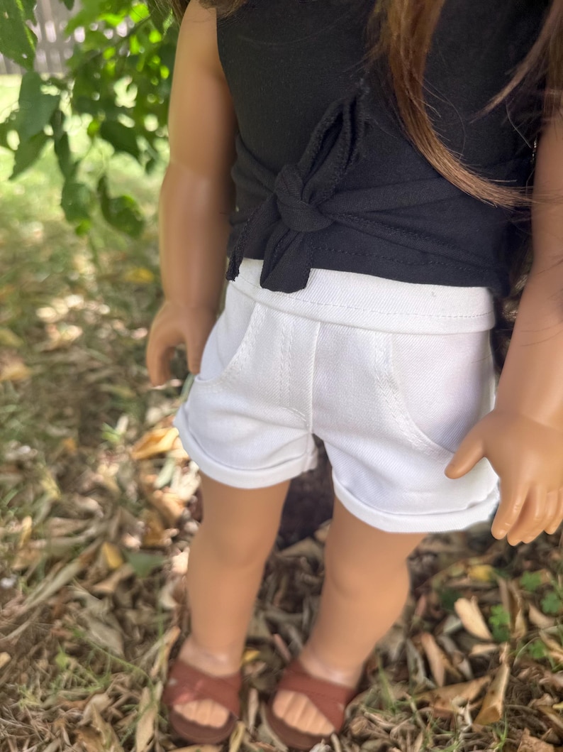 Peut inclure: Une poup&eacute;e v&ecirc;tue d'un haut noir nou&eacute; &agrave; la taille et d'un short blanc avec des poches. La poup&eacute;e porte &eacute;galement des sandales marron. La tenue est adapt&eacute;e &agrave; une poup&eacute;e.