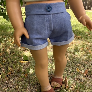 Peut inclure: Shorts en jean bleu avec fermeture boutonn&eacute;e et revers aux ourlets. Le short est associ&eacute; &agrave; un haut court vert clair avec un motif d'abeille. La poup&eacute;e porte des sandales marron. La tenue est con&ccedil;ue pour une poup&eacute;e.