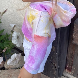 K&ouml;nnte beinhalten: Ein rosa, gelber und orangefarbener Tie-Dye-Hoodie mit Kapuze. Der Hoodie ist aus weichem, bequemem Material gefertigt und hat eine lockere Passform.