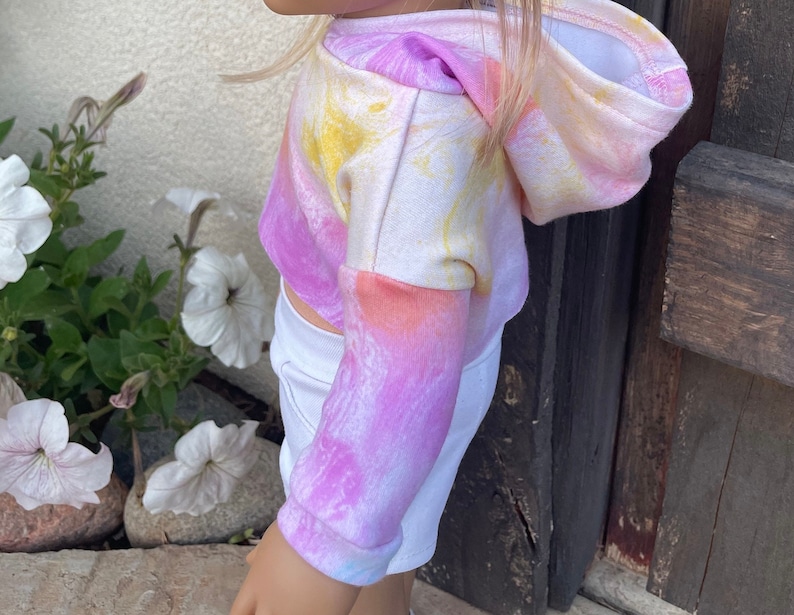 K&ouml;nnte beinhalten: Ein rosa, gelber und orangefarbener Tie-Dye-Hoodie mit Kapuze. Der Hoodie ist aus weichem, bequemem Material gefertigt und hat eine lockere Passform.