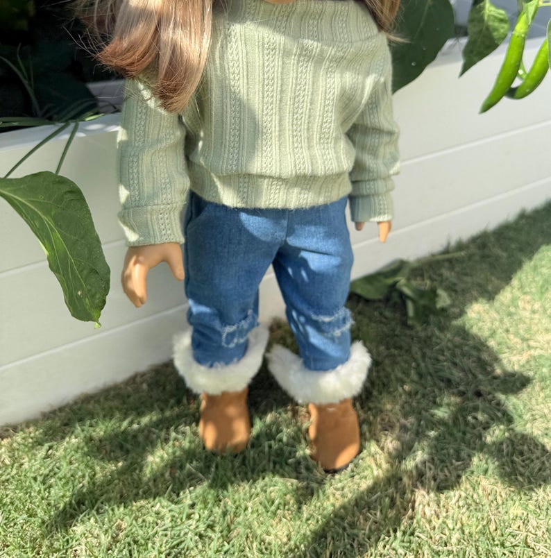Puede incluir: Una mu&ntilde;eca con un su&eacute;ter verde claro, pantalones vaqueros azules y botas marrones con ribete de piel blanca.