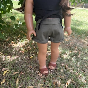 Peut inclure: Une poup&eacute;e v&ecirc;tue d'un haut noir avec une attache crois&eacute;e et d'un short vert olive. La poup&eacute;e porte &eacute;galement des sandales marron. La poup&eacute;e est debout sur de l'herbe.