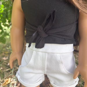 Peut inclure: Un haut noir sans manches avec un d&eacute;tail nou&eacute; et un short en jean blanc. Le short a des poches et des revers. La tenue est con&ccedil;ue pour une poup&eacute;e.