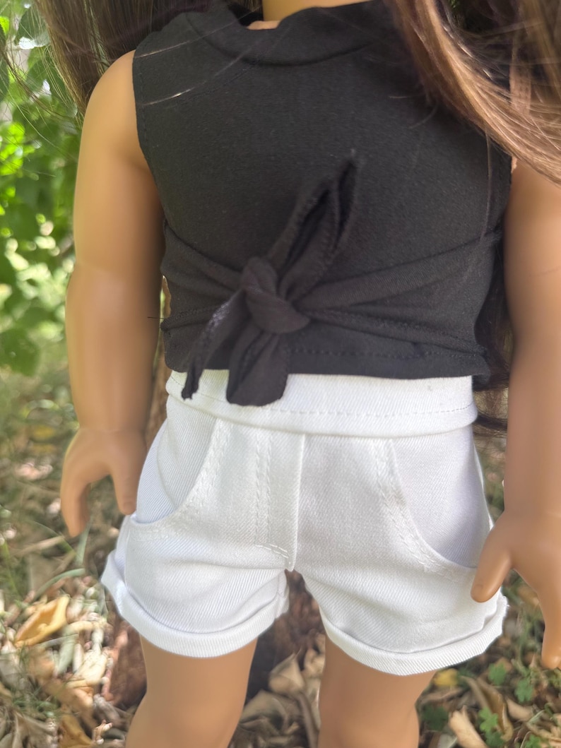 Peut inclure: Un haut noir sans manches avec un d&eacute;tail nou&eacute; et un short en jean blanc. Le short a des poches et des revers. La tenue est con&ccedil;ue pour une poup&eacute;e.
