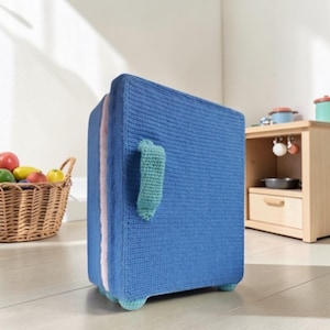 May include: A rectangular toy refrigerator made of blue crocheted yarn with a light pink side panel and a mint green crocheted handle. The structure stands on four small mint green crocheted feet and features a textured, hand-stitched appearance.