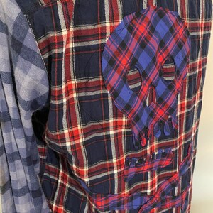 May include: A blue and red checked flannel shirt with a blue and red skull patch sewn on the back. The skull patch has a frayed edge.