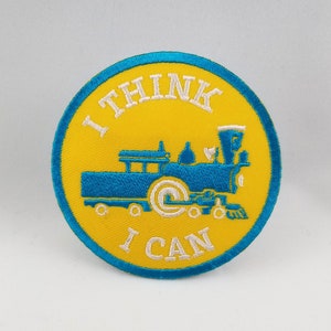Puede incluir: Un parche bordado amarillo y azul con un tren y el texto "I think I can".