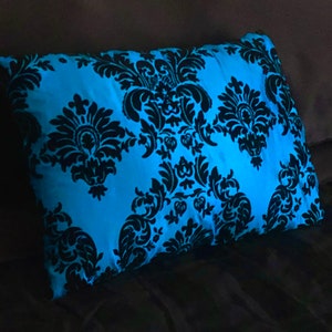 May include: A blue pillow with a black damask pattern. The pillow is glowing in the dark.