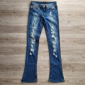 May include: Distressed blue denim jeans with a bootcut leg style. The jeans have several rips and tears throughout the fabric.
