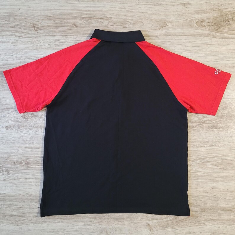 K&ouml;nnte beinhalten: Schwarzes Poloshirt mit roten &Auml;rmeln. Das Shirt hat einen Kragen und kurze &Auml;rmel. Die R&uuml;ckansicht zeigt die kontrastierenden Farben und das Design. Das Shirt ist aus leichtem Material gefertigt.