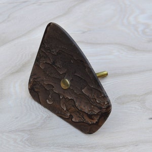 May include: A brown, triangular-shaped door knob with a textured surface and a gold metal accent.