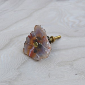 May include: A brown, white, and orange agate knob with a gold metal base. The knob is shaped like a rough, natural stone.
