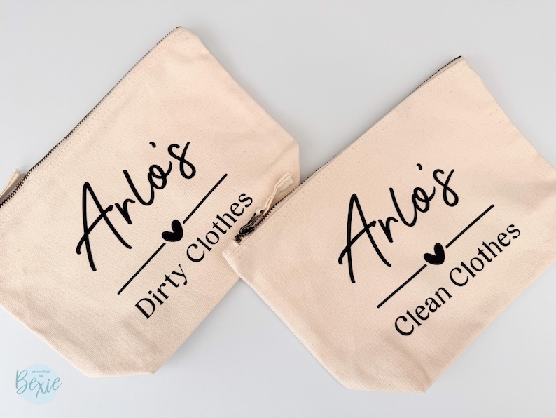 Peut inclure: Deux pochettes zipp&eacute;es en toile beige. L'une porte l'inscription "Arlo's Dirty Clothes" et l'autre "Arlo's Clean Clothes" en &eacute;criture noire. Un c&oelig;ur noir et un trait sont sous le nom. Les pochettes sont sur fond blanc.